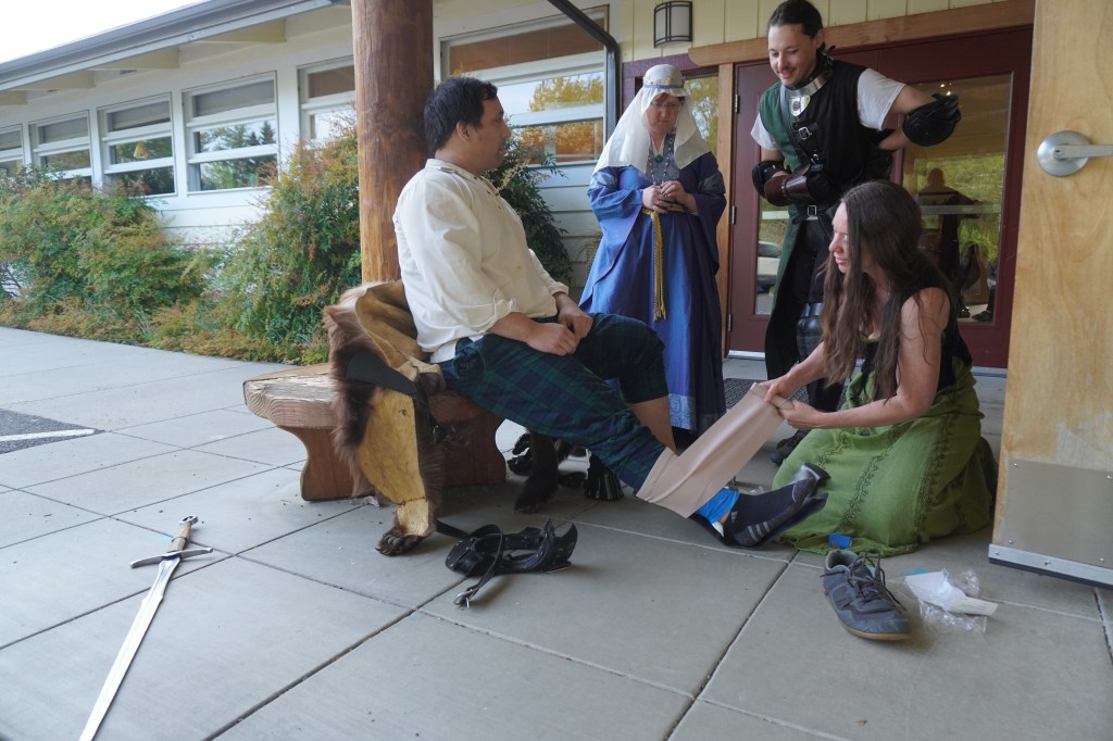 Josh Campbell gets his leg and foot wrapped by an ER nurse on site at Siskiyou School in Ashland, Oregon, while Cody Williams checks on him and Dawn Dille calls the Ashland ER. Sword, gorget, and shoe are seen on the ground. April 16, 2026.